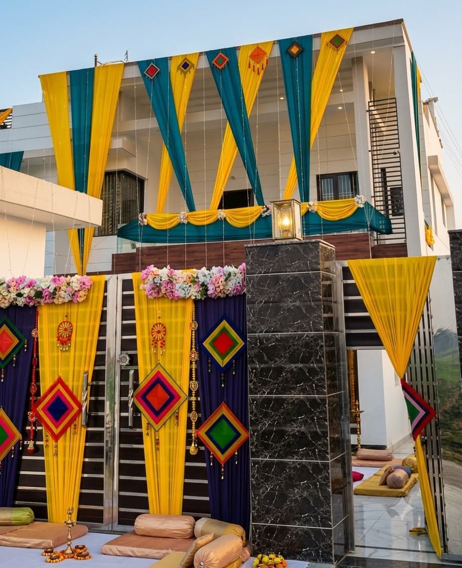 House front dressed for a Haldi ceremony with yellow and teal drapes, colourful diamond motifs and floral garlands