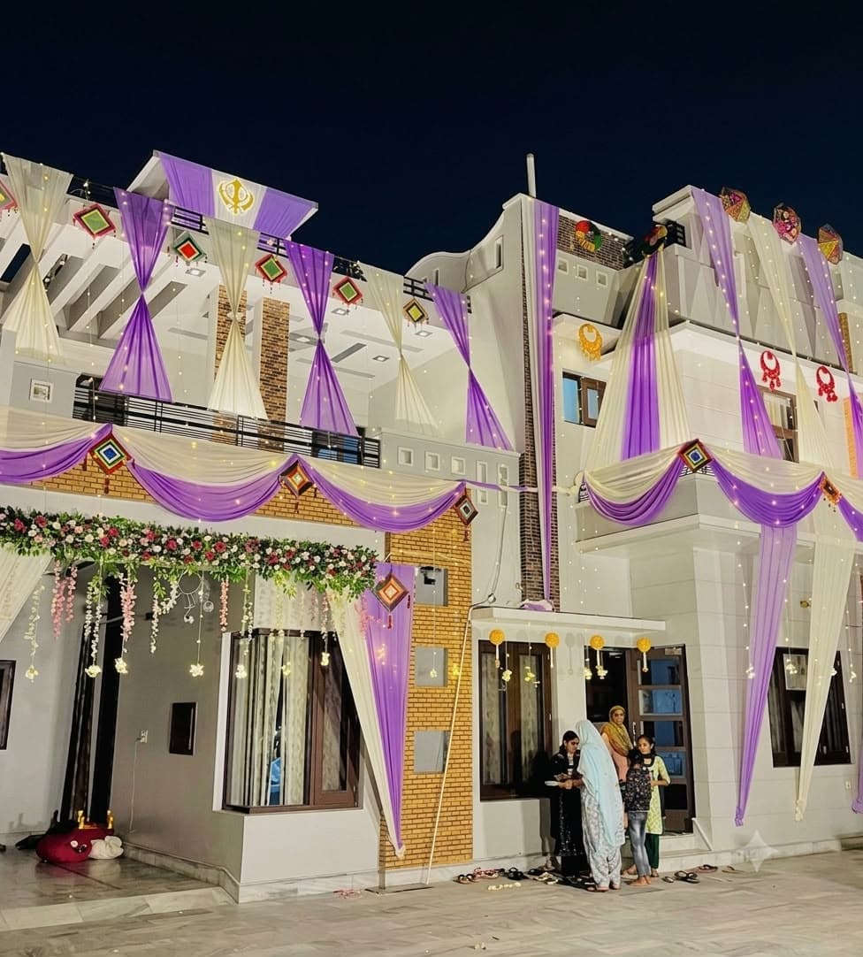 House front decorated at night with purple and white drapes, floral garlands and fairy lights for a wedding function