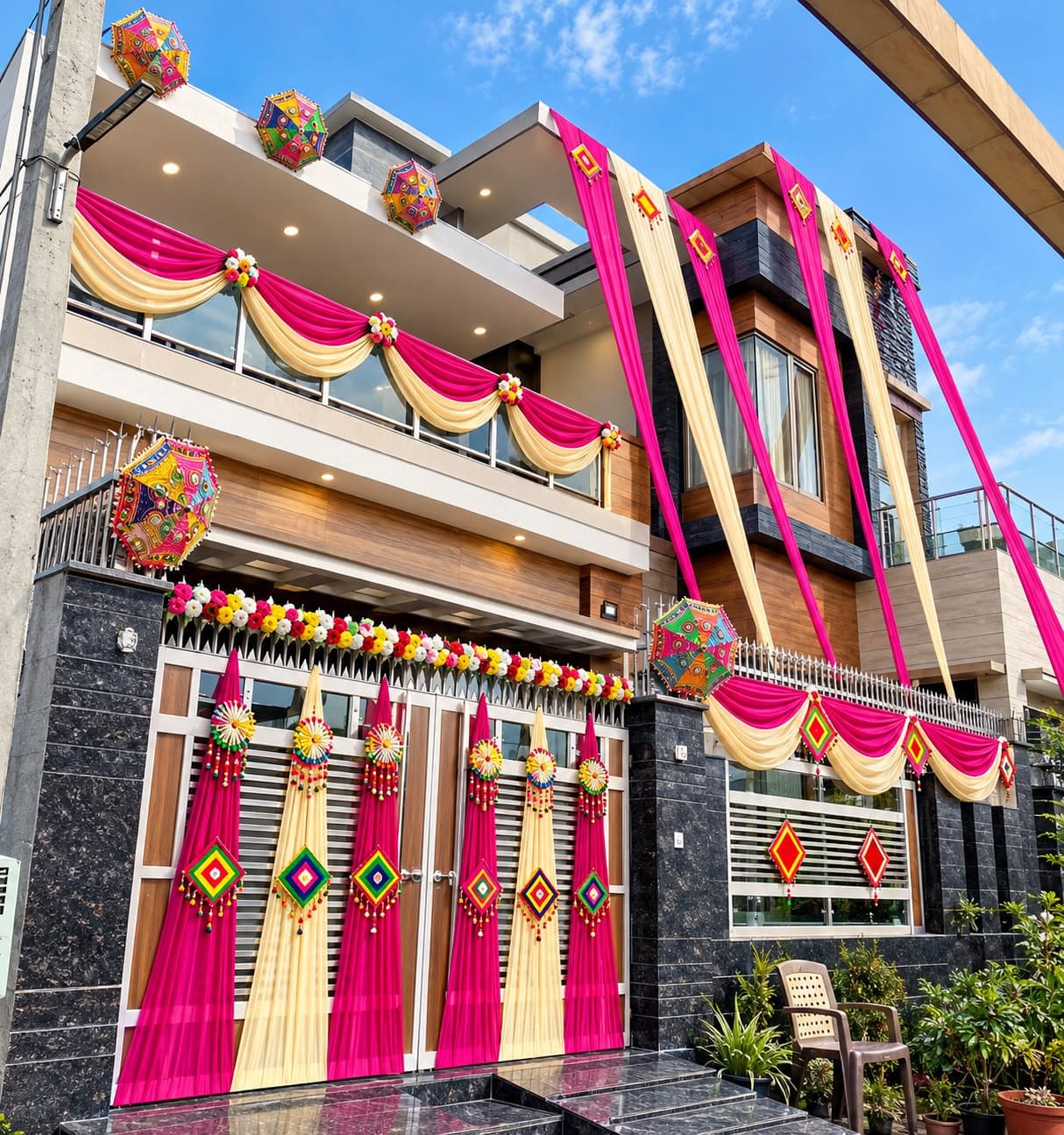 House front decorated with vibrant pink and cream drapes, Rajasthani umbrella props and colourful floral strings for a Haldi function