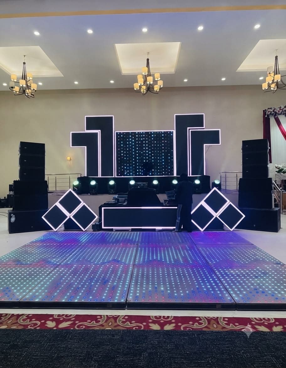 DJ stage with line-array speakers, an LED backdrop and a lit LED dance floor in a banquet hall