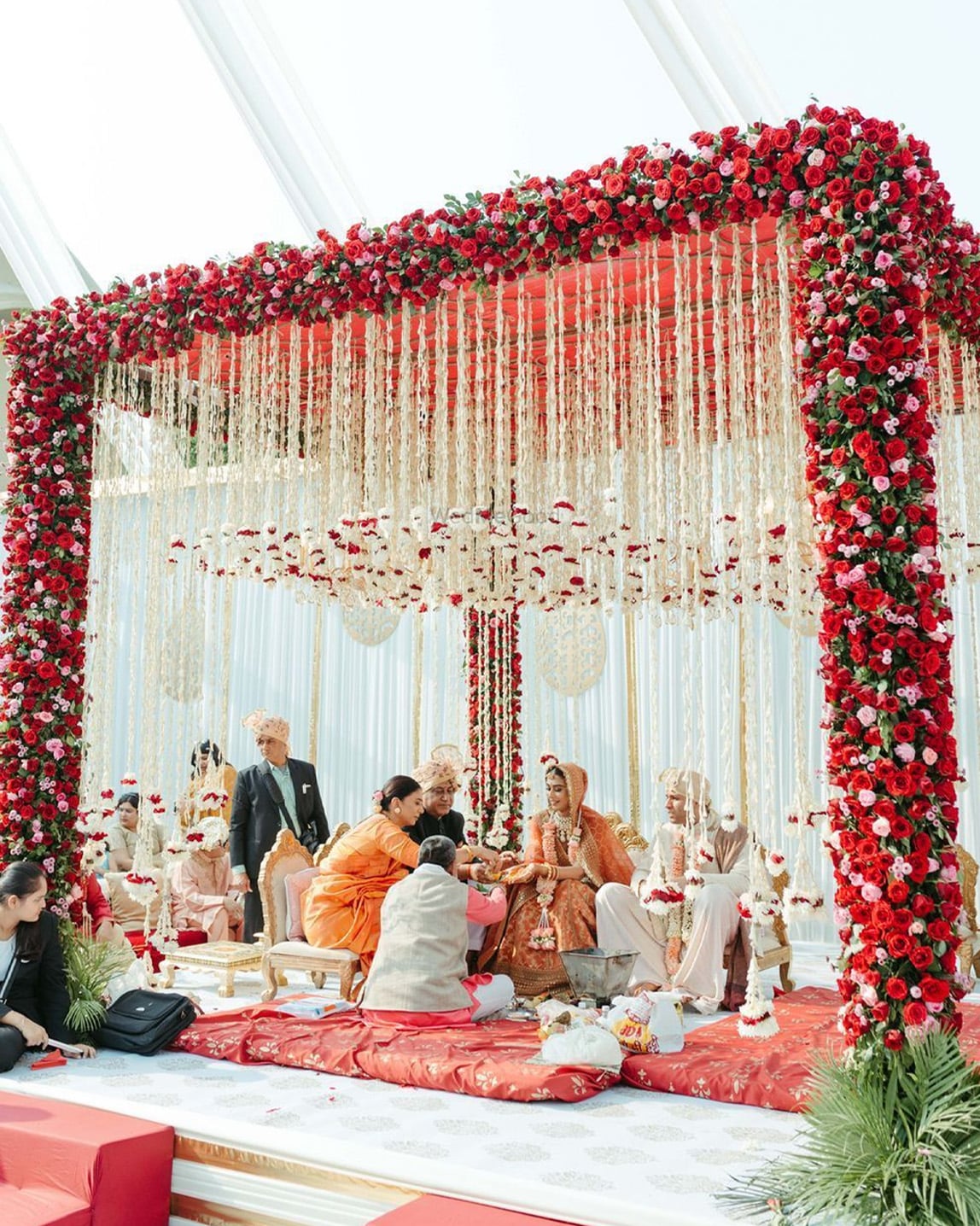 Wedding mandap draped in red and blush roses with hanging floral strings during the ceremony